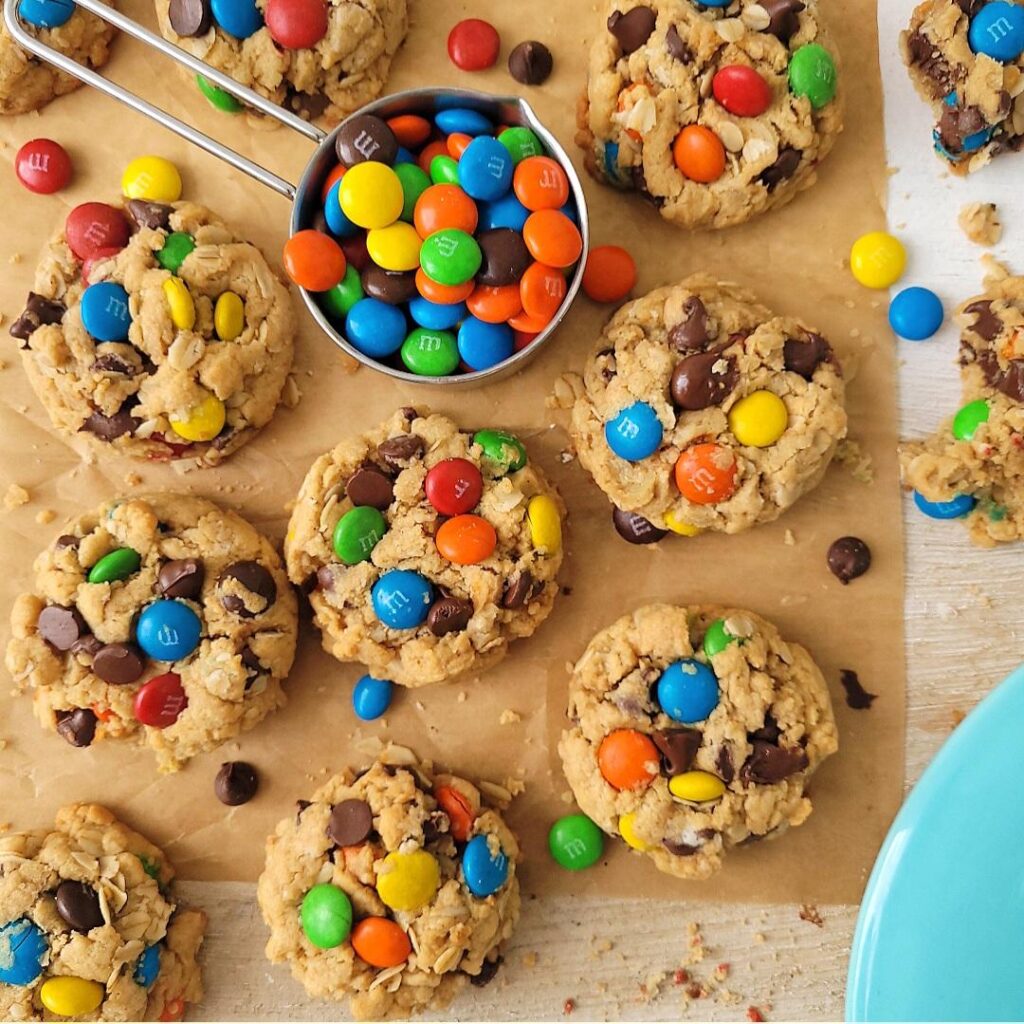 easy monster cookies. top down view of cookies with a measuring cup full of colorful m& m candies. 