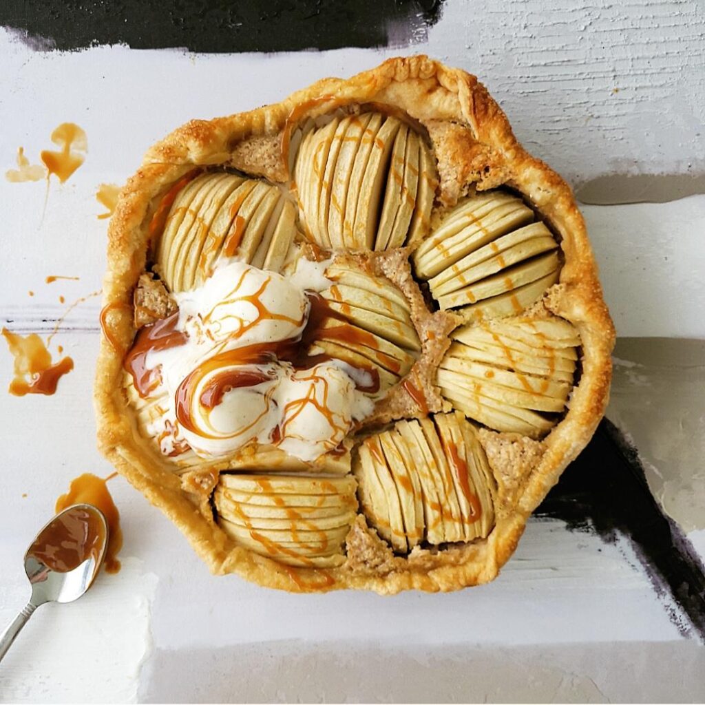 puff pastry apple tart top down view. pie is garnished with scoops of vanilla ice cream and drizzles of caramel