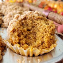 pumpkin banana muffin with crumble topping in a muffin tin. muffin has been bitten so you can see the inner pumpkin colored crumb.