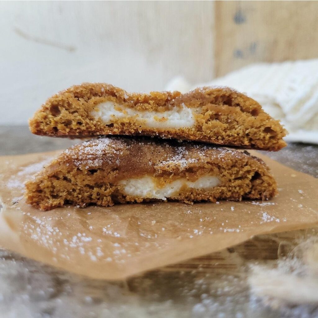 two stack of pumpkin cheesecake cookies that have been cut in half and sprinkled with cinnamon sugar so you can see the inner pumpkin crumb and cheesecake filling. 