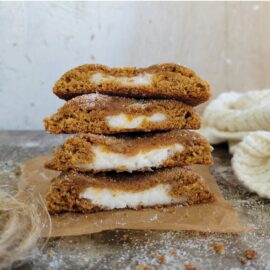 pumpkin cheesecake cookies stacked 4 high. cookies have been cut in half so you can see the inner pumpkin crumb and cheesecake filled center. side view.