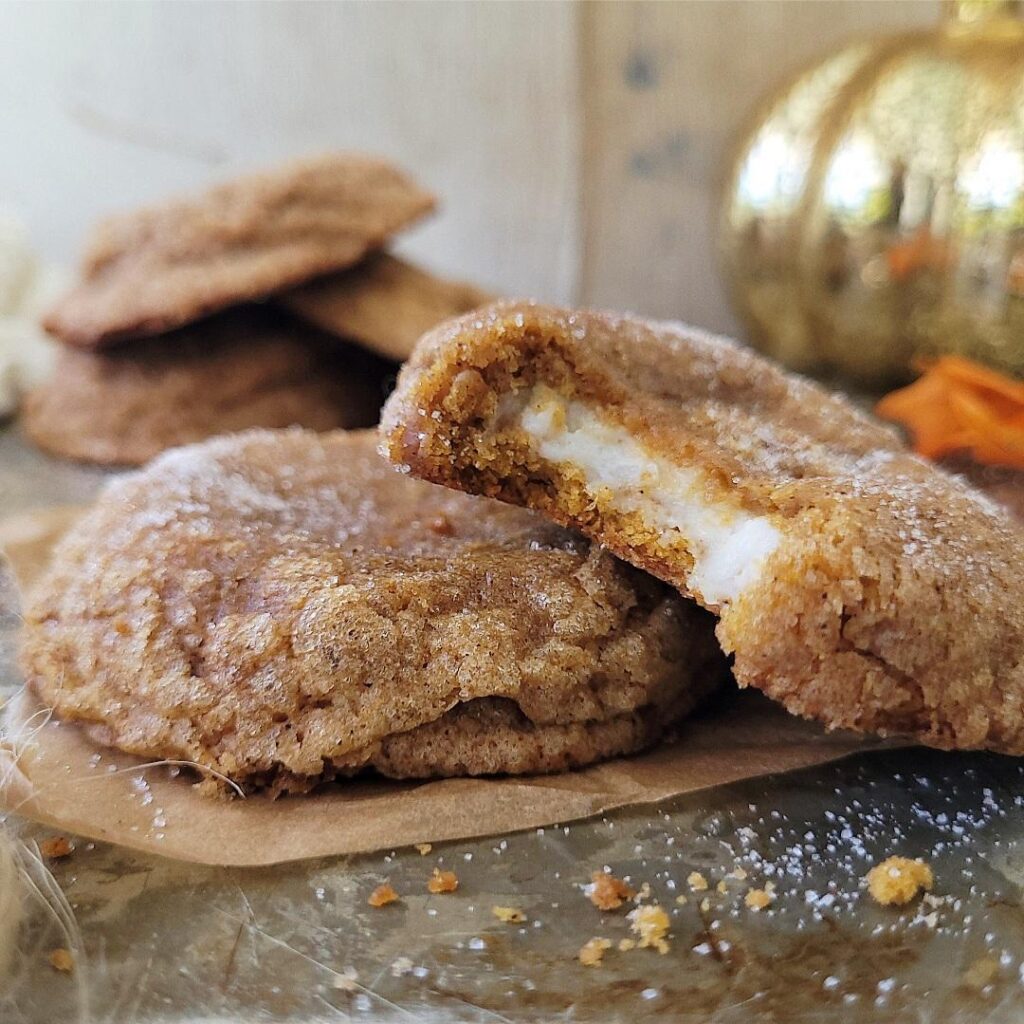pumpkin cheesecake cookies. stuffed cookie is bitten so you can see the inner cream cheese layer that's surrounded by pumpkin cookie. 