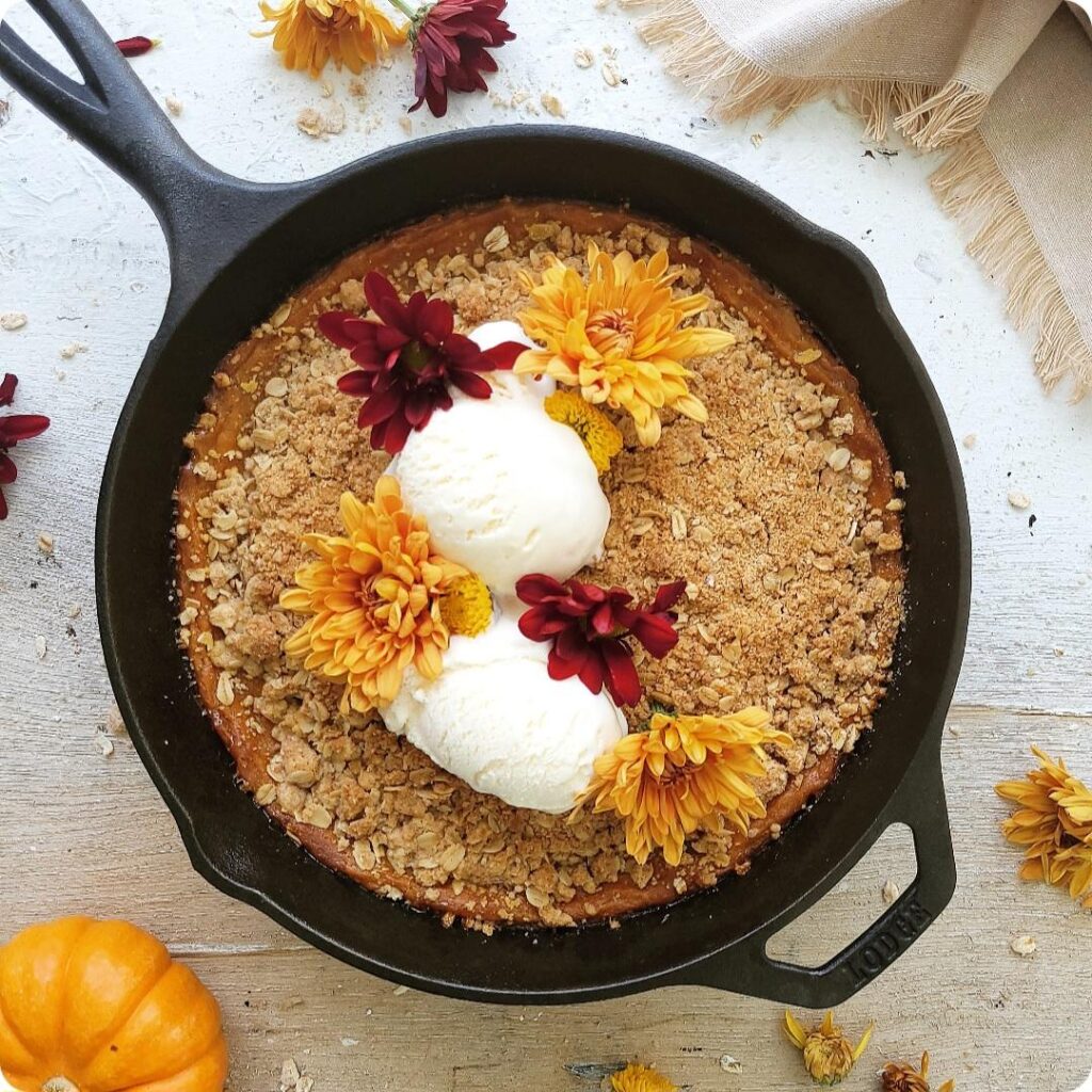 pumpkin crisp baked in a cast iron skillet. top down view of crisp garnished with fall flowers and two scoops of vanilla ice cream. 