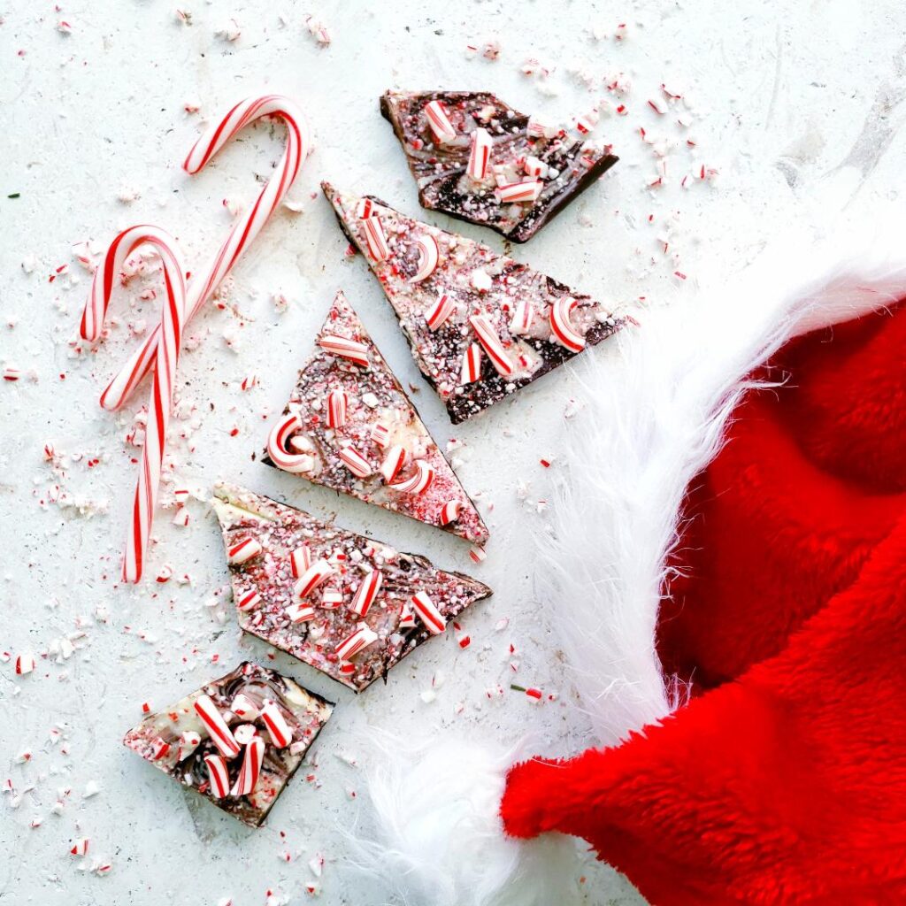 boozy peppermint bark. top down view of homemade peppermint bark broken into big pieces. bark is topped with broken candy canes. surface is white marble and is styled with two candy canes and a santa hat. 