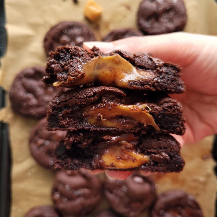 chocolate caramel cookies. close of view of hand holding three cookies cut in half so you can see the ooey gooey centers.