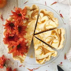 cream cheese pumpkin pie. top down view of pie in a glass pie plate. pumpkin pie is swirled with cream cheese and garnished with pretty fall flowers. three slices have been cut but are still in the pie plate.
