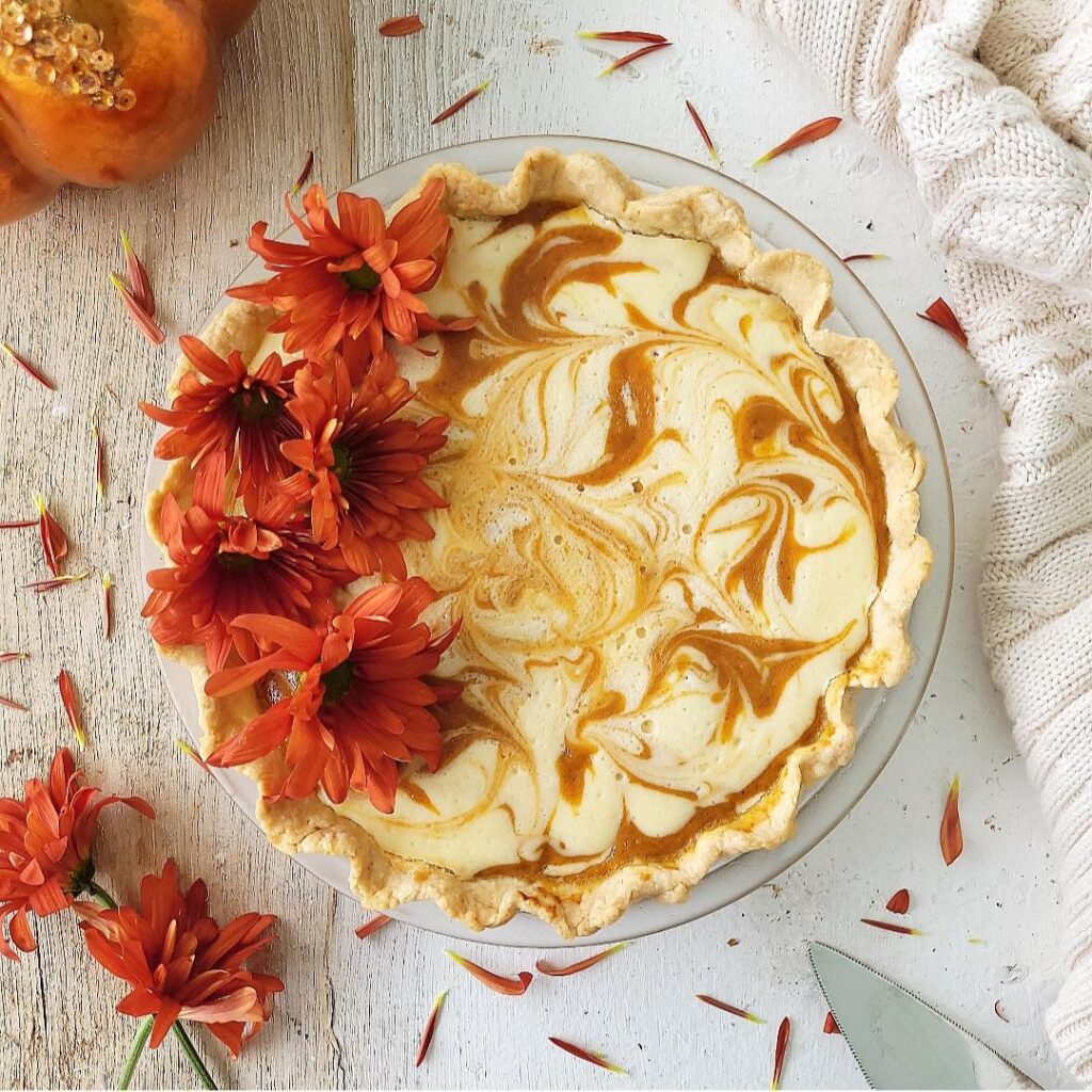 cream cheese pumpkin pie uncut. top down version of pie in a glass pie dish garnished with fresh fall flowers on the left side of the pie. 