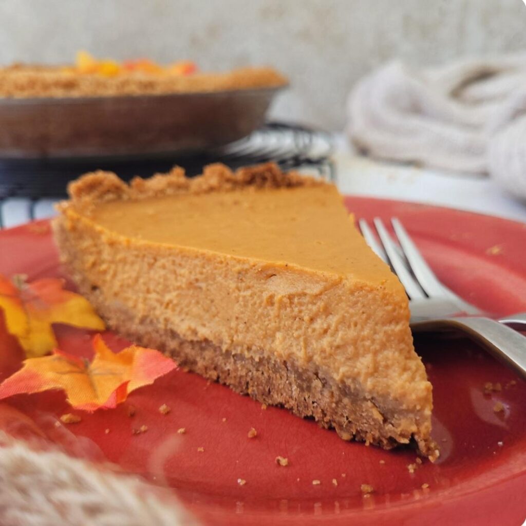 graham cracker crust pumpkin pie. side view of pie slice on a red plate with tiny fall leaves and two forks.