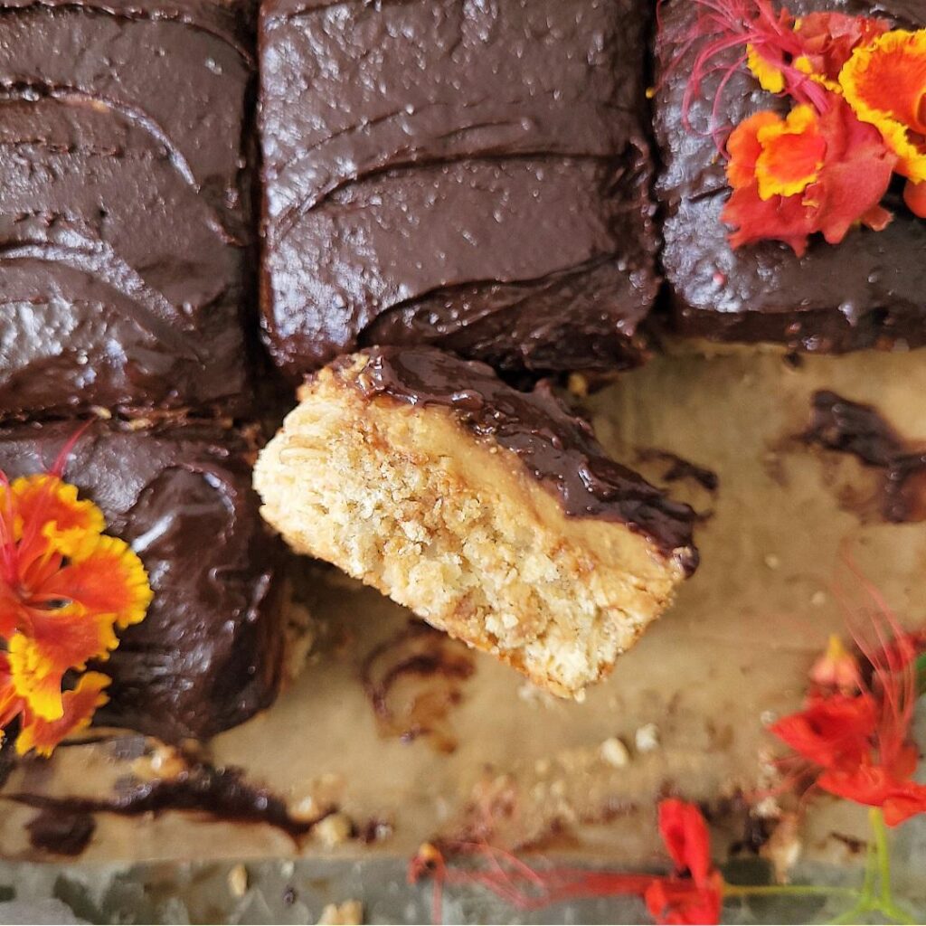 peanut butter oatmeal bars. top down view of cut bars with red and orange flowers on the chocolate layer. one cut bar is turned on its side so you can see the cookie, peanut butter and chocolate layers.