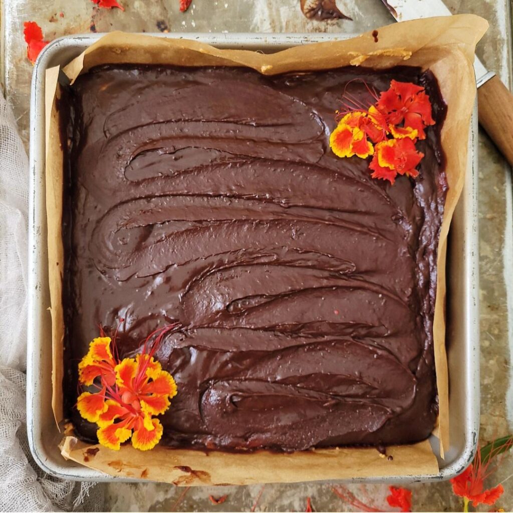 chocolate peanut butter oatmeal bars. top down view of uncut bars in a square baking pan. top is swirled with chocolate and garnished with orange and yellow flowers in the corners. 
