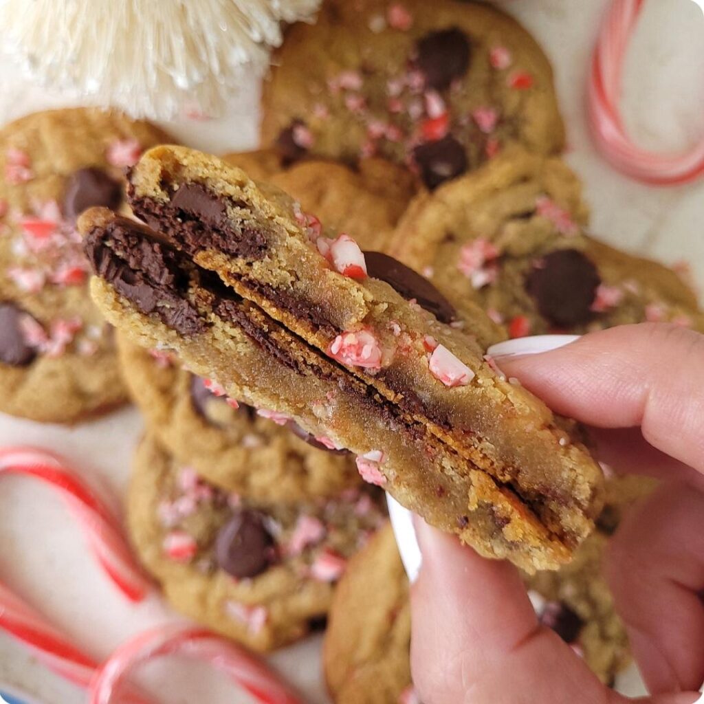 peppermint chocolate chip cookies. close up view of two halves of the cookies held together so you can see the inner crumb, chocolate chips and candy cane pieces.