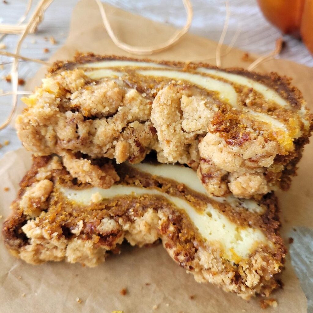 pumpkin cream cheese bread. two slices of pumpkin bread swirled with cream cheese stacked on top of each other. bread is topped with a crunchy crumb topping. 