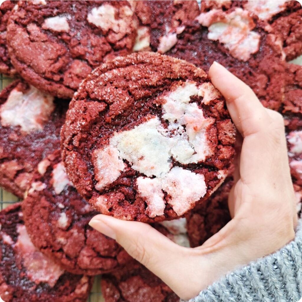 red velvet cookies with cream cheese. close up view of a hand holding a crackly red cookie swirled with cream cheese. 
