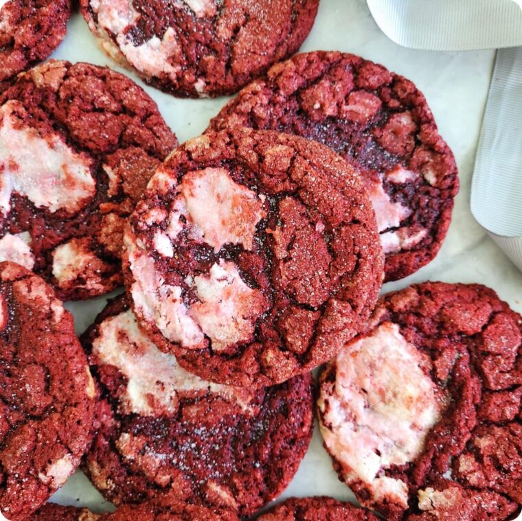 flat pile of crackly red velvet cookies with patches of cream cheese baked into the dough.