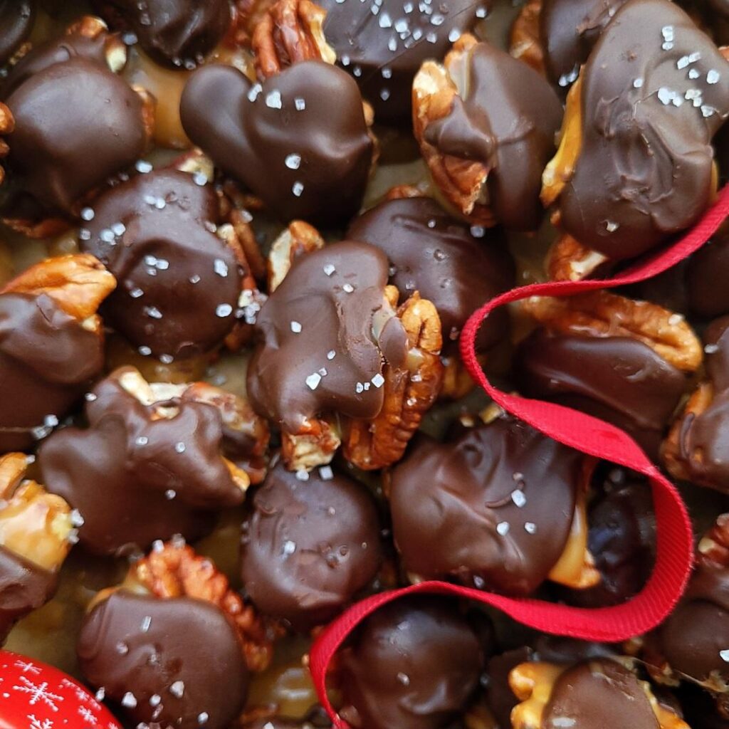 dark chocolate caramel turtles. close up view of a pile of turtles sprinkled with sea salt and styled with a red ribbon. 