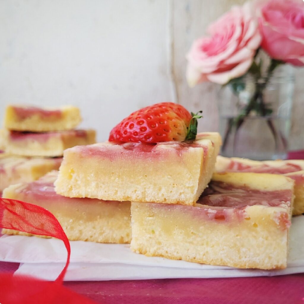 strawberry blondies. pile of strawberry blondie squares piled atop each other. side view so you can see the inner crumb and the strawberry swirl layer on top. 