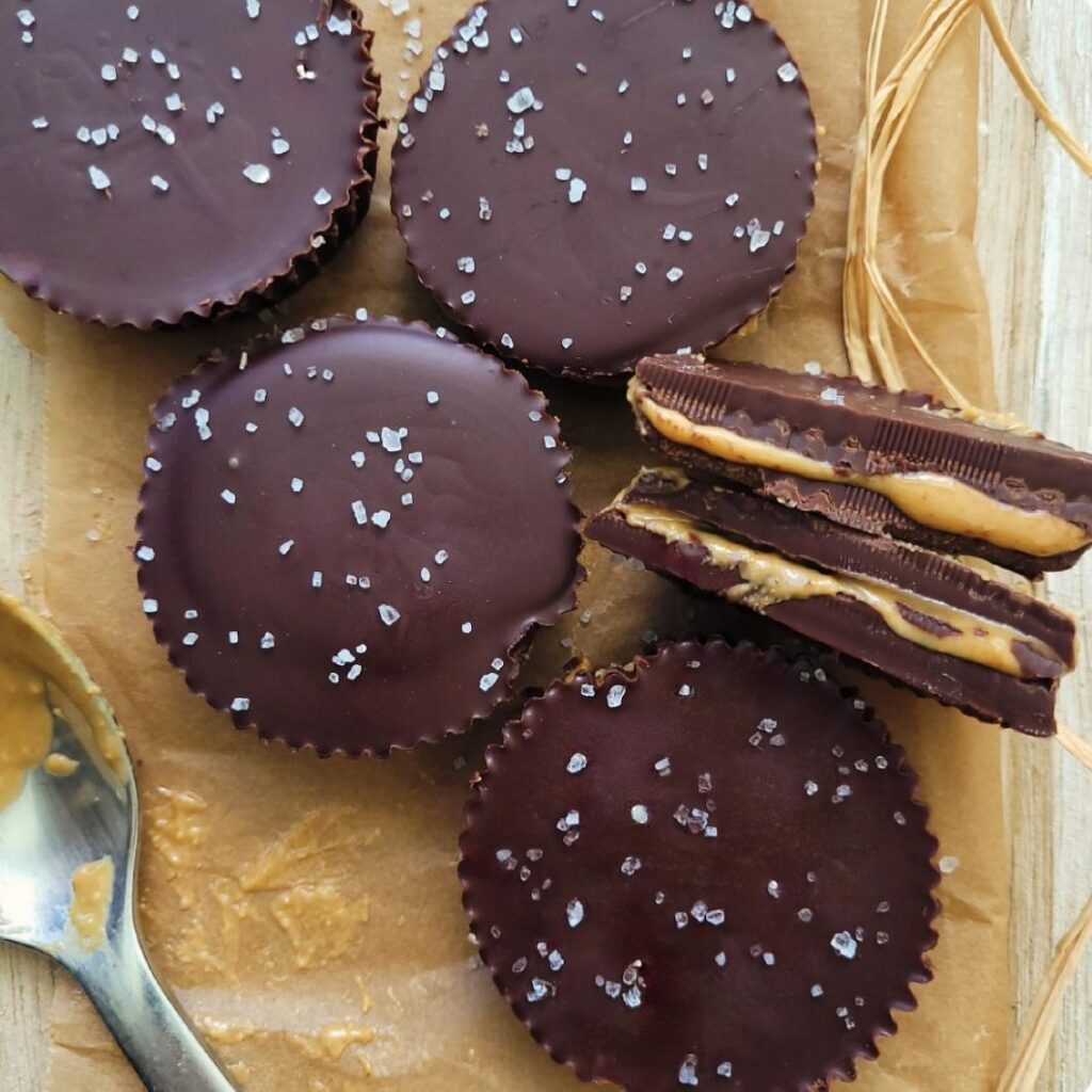 salted dark chocolate peanut butter cups. top down view of 5 homemade peanut butter cups. one pb cup is cut in half and turned on its side so you can see the inner layer of peanut butter