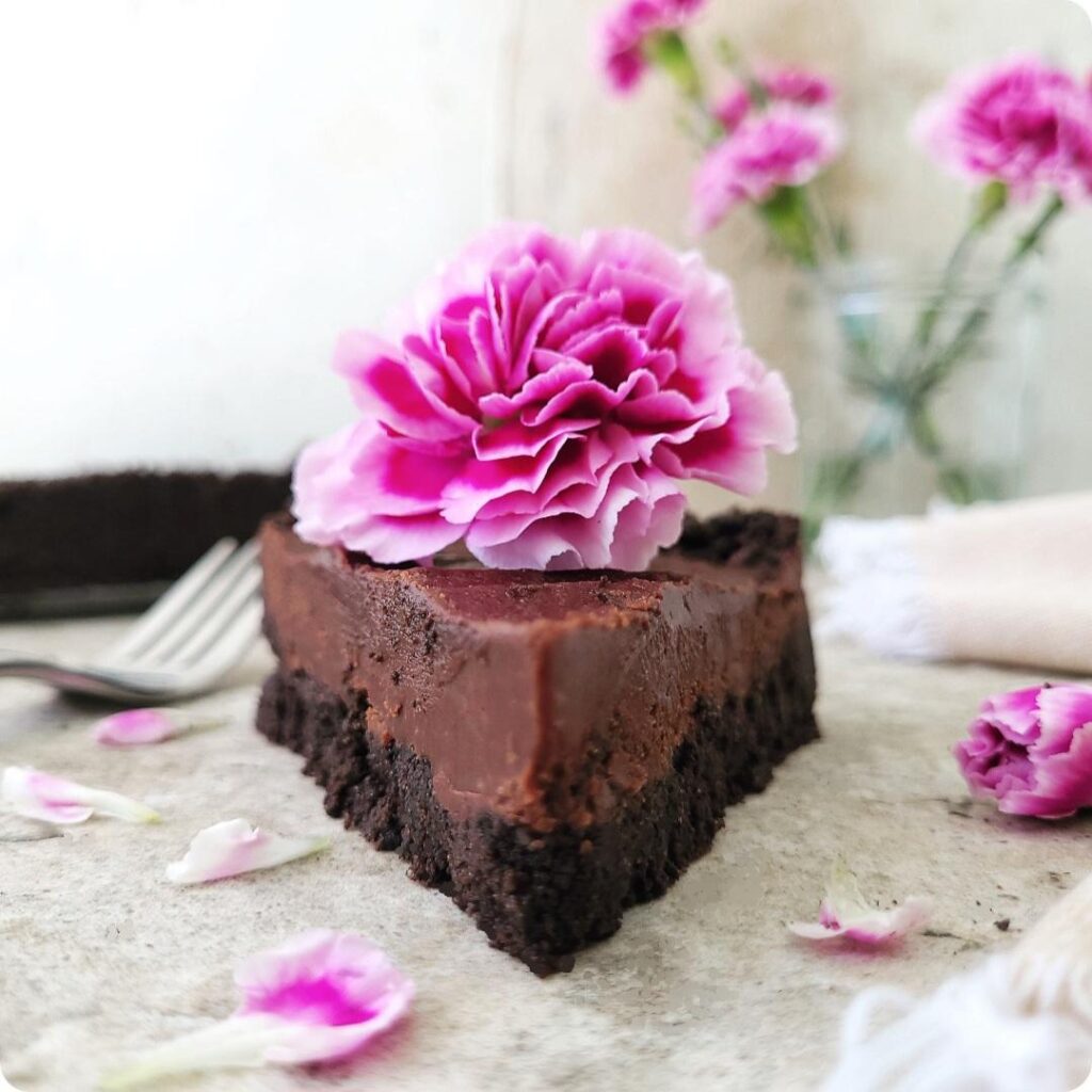 no bake nutella pie. close up side view of a slice topped with a purple carnation so you can see the thick layer of oreo cookie crust and the layer of nutella ganache filling. 