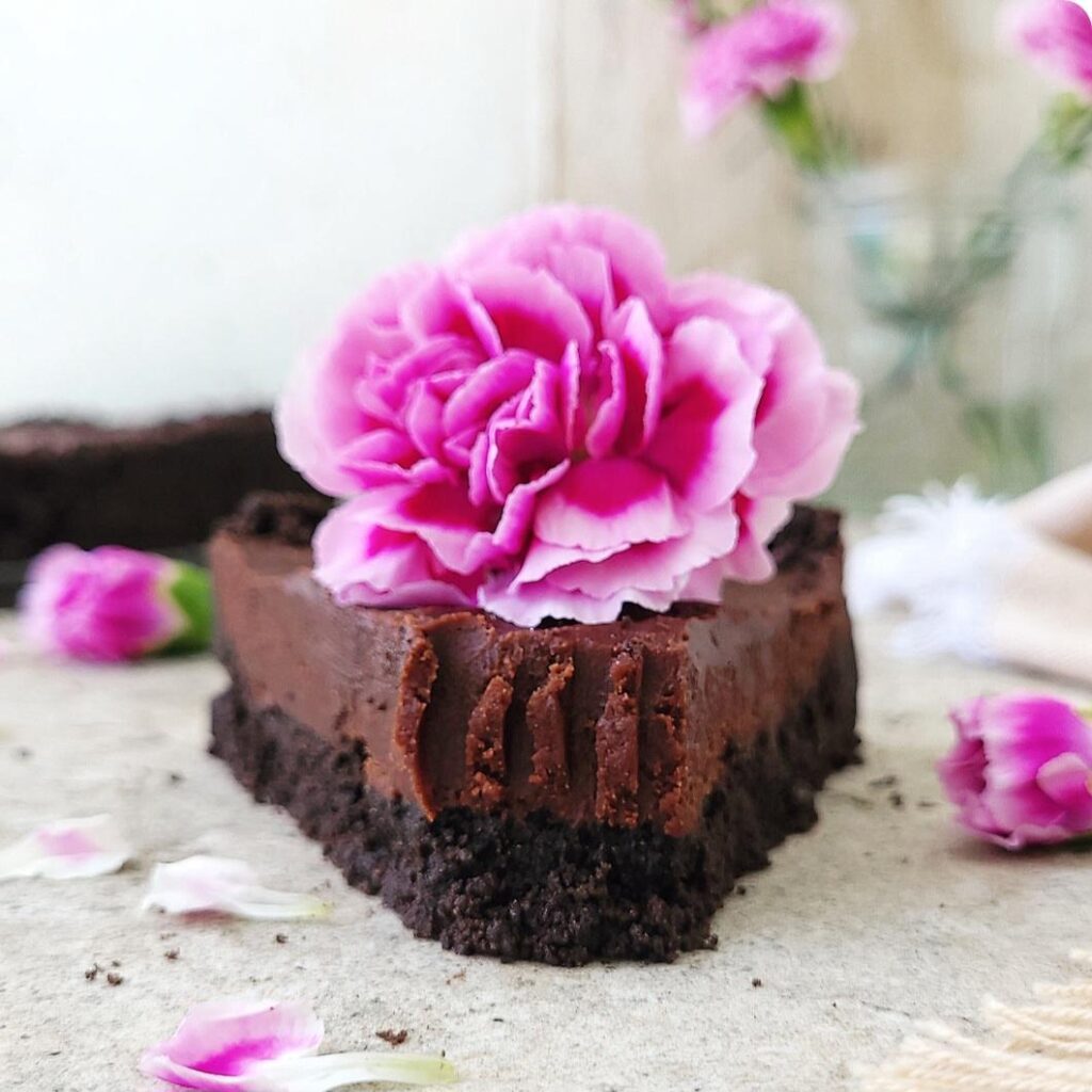 no bake nutella pie with oreo cookie crust. close up side view of a slice of pie with a big purple carnation on top. you can see the grooves from a fork in the tip of the pie where a bite was eaten. 