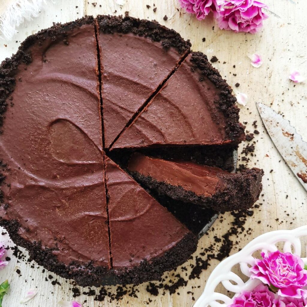 no bake nutella pie. top down view of pie with 4 slices cut. one slices is on it's side so you can see the oreo cookie layer and the layer of chocolate nutella ganache. 