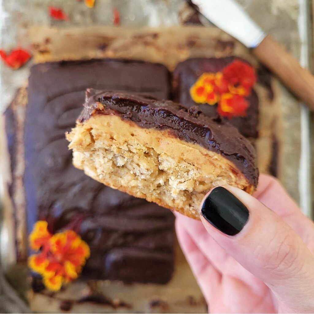 peanut butter oatmeal bars topped with chocolate. close up view of a hand holding a peanut butter oatmeal bar so you can see the layers of oatmeal, peanut butter and chocolate.