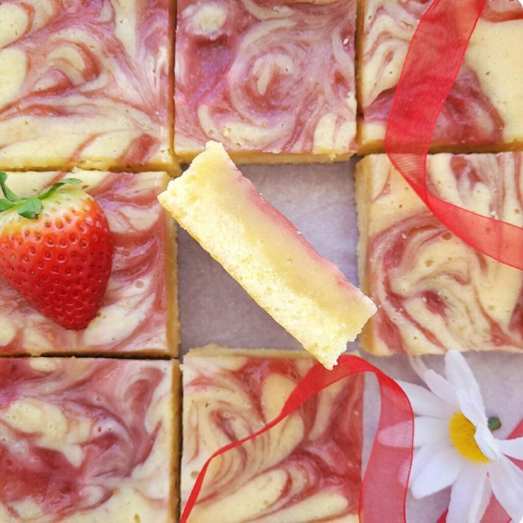 strawberry blondies. top down view of strawberry swirl blondies cut into squares. the middle square is flipped on its side and facing up so you can see the inner crumb and top layer of strawberry swirl. 