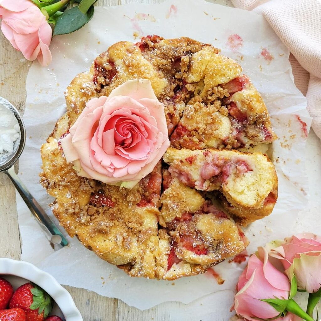 strawberry crumb cake. top down view of cake with three slices cut. one slice is turned on its side so you can see the inner crumb and strawberries. cake is topped with a pale pink rose. 