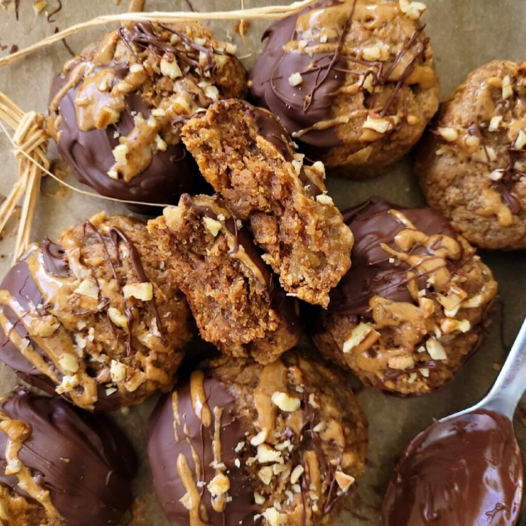 banana almond butter cookies. top down view of these eggless cookies on a baking sheet. one cookie is split and half and turned on it's side to see the inner crumb. 