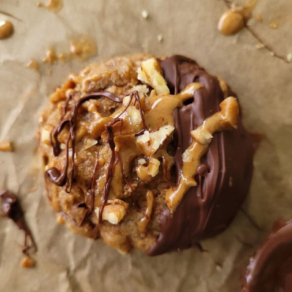 banana almond butter cookie. close up view of vegan cookie topped with melted chocolate, almond butter drizzle and chopped pecans. 