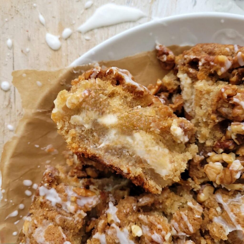 walnut streusel banana coffee cake swirled with cream cheese. top down, close up view of a square slice of cake turned on its side so you can see the inner crumb and cream cheese layer.