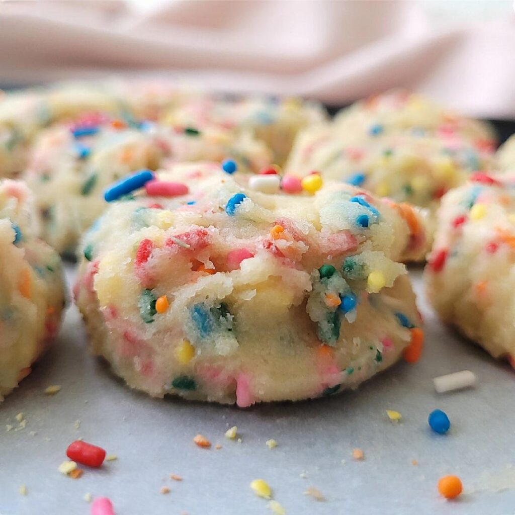 funfetti cookies. close up view of funfetti cookie dough balls on a baking sheet. dough is filled with colorful sprinkles inside and out. 