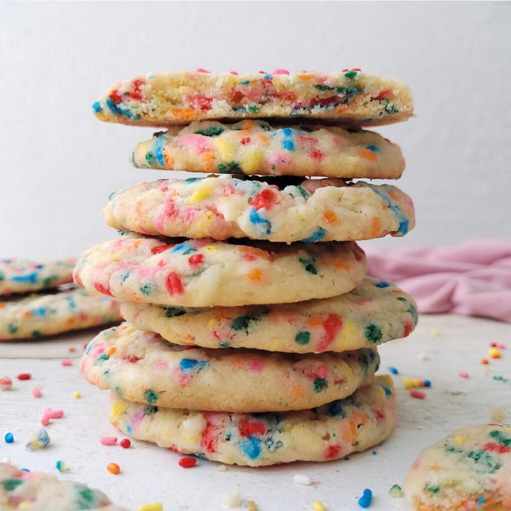 side view of 7 funfetti cookies stacked atop each other. image is styled with funfetti sprinkles. 