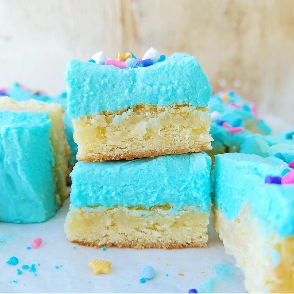 frosted sugar cookie bars. side view of two bars stacked atop each other. each bar is frosted with blue buttercream and topped with colorful sprinkles. 