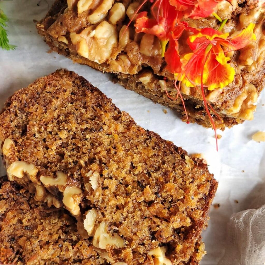 carrot bread with walnuts. top down, close up view of bread loaf with two slices cut and facing up so you can see the walnut topping and the moist inner crumbs. 
