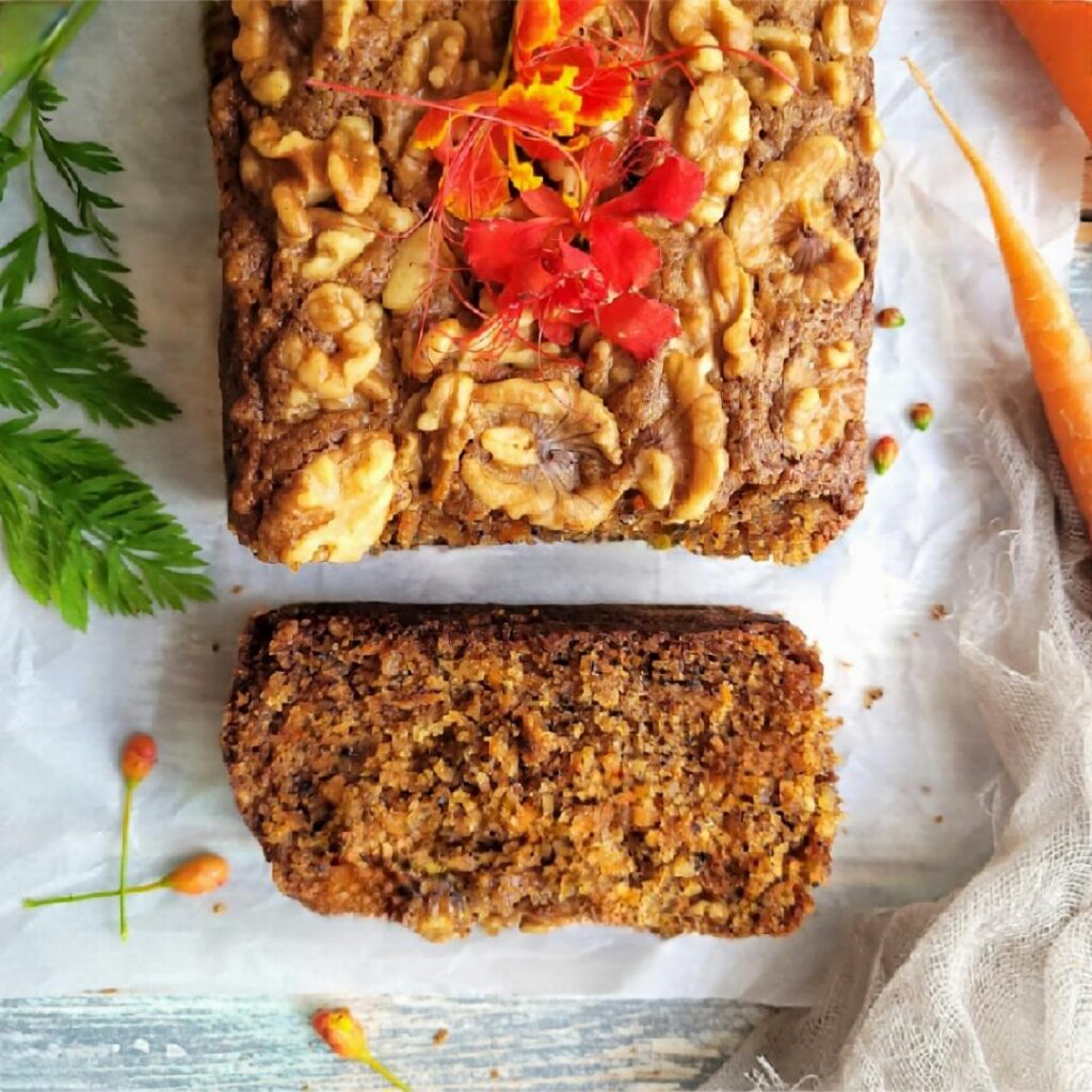 carrot bread with walnuts. top down view of loaf. one slice has been cut and is resting flat so you can see the moist crumb. 