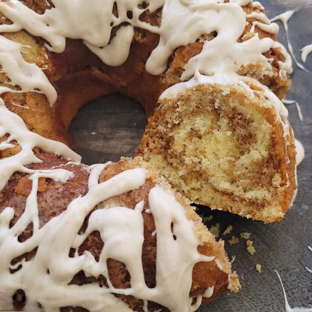 cinnamon bundt cake. top down view of cake with one slice cut and facing up so you can see the cinnamon swirl cake crumbs. 