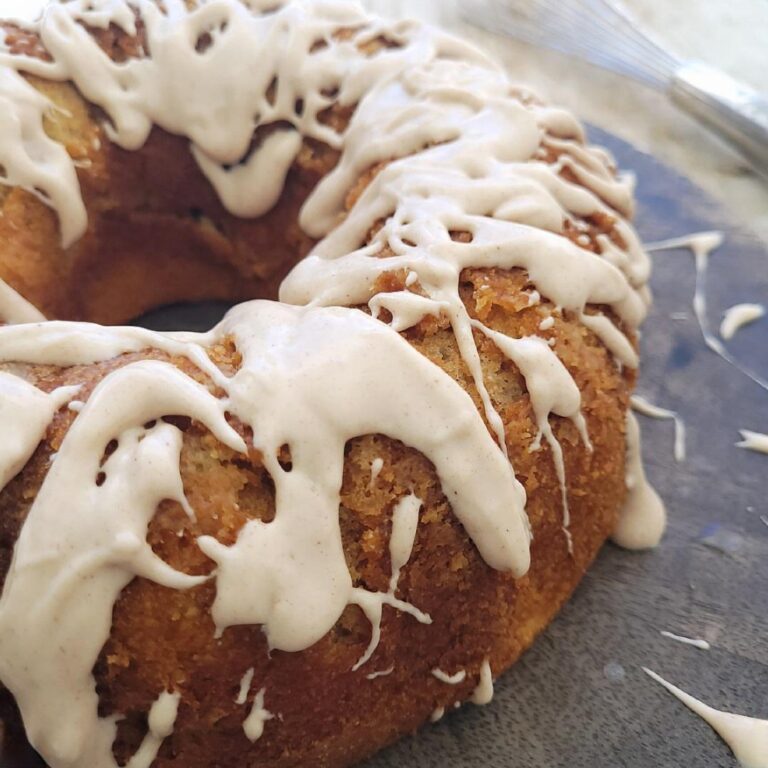 cinnamon bundt cake dripping with cinnamon cream cheese glaze. top down view of the cake on a dark wood charger splattered with glaze.