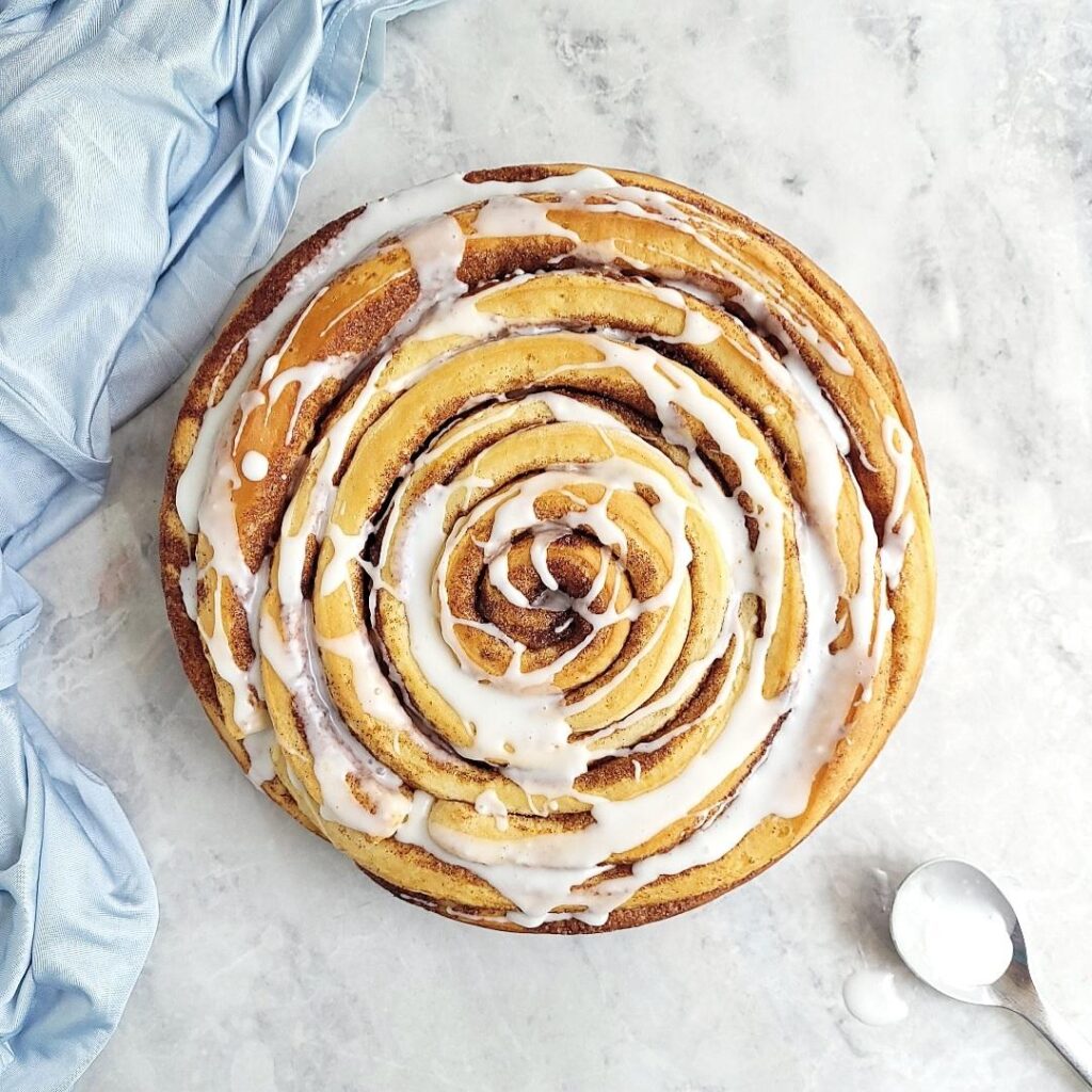 giant cinnamon roll. top down view of cinnamon roll glazed with vanilla icing on a gray marble surface. 