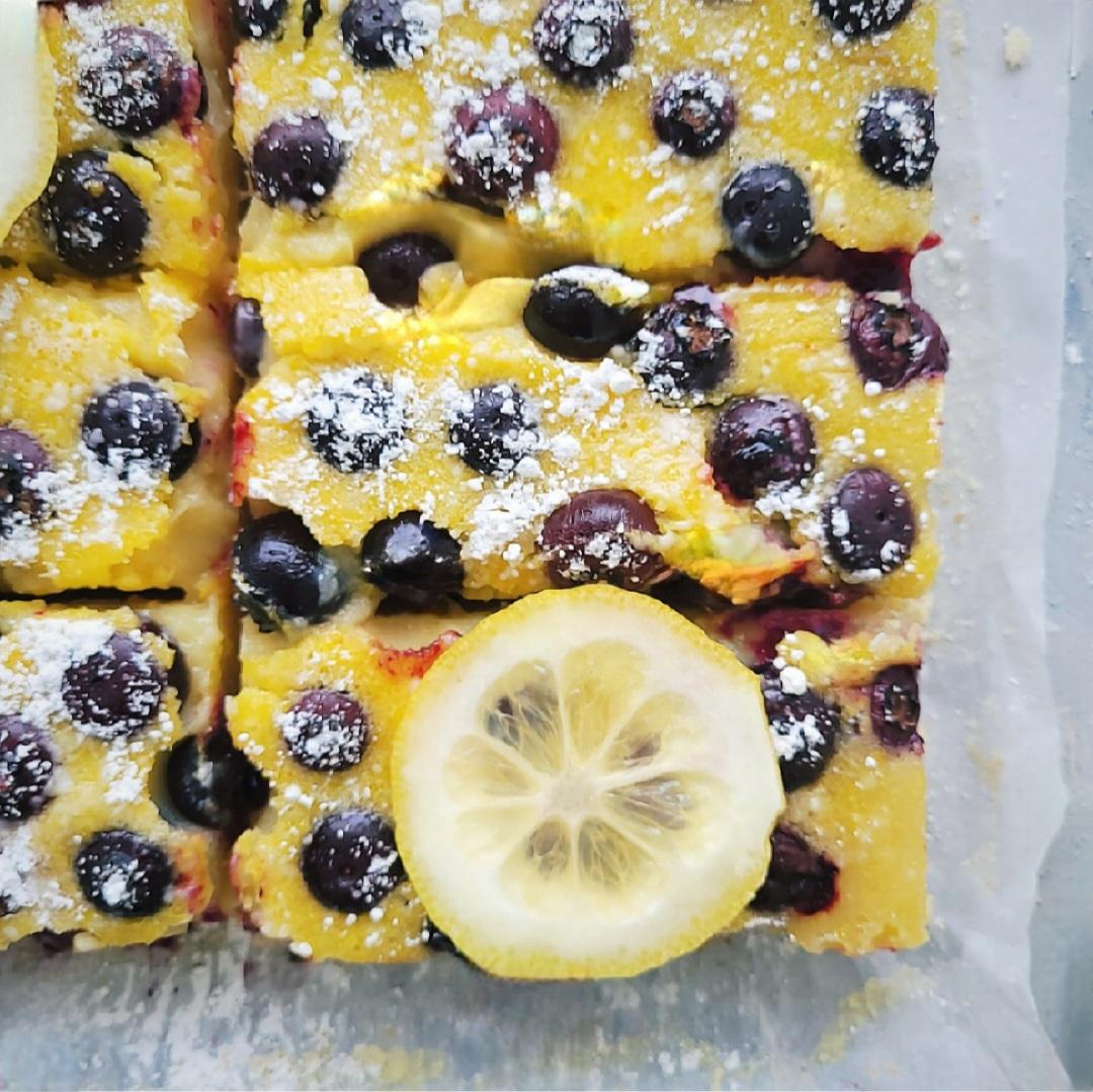 blueberry lemon shortbread. top down close up view of shortbread cut into rectangles. one bar is topped with a thinly sliced lemon. 