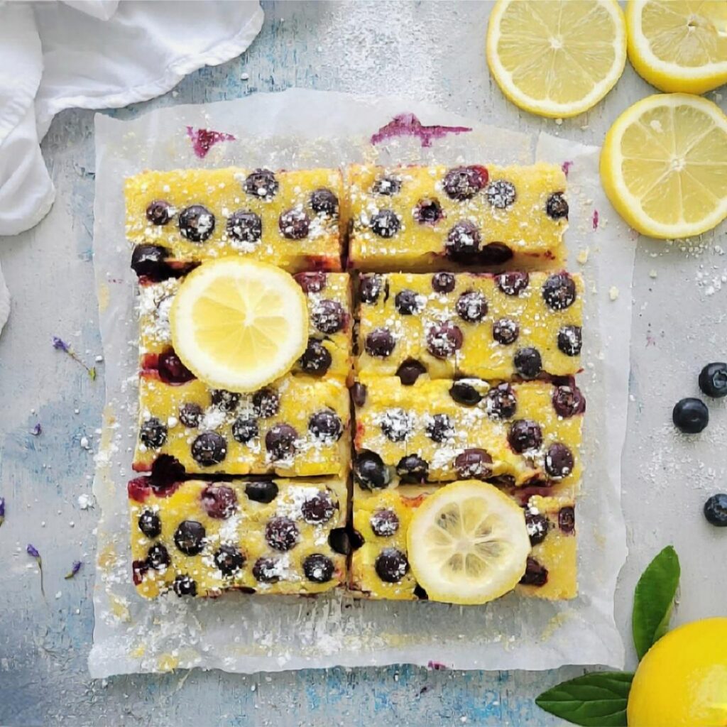 blueberry lemon shortbread bars. top down view of a batch of shortbread cut into 8 rectangular bars and garnished with 2 slices of lemon. 