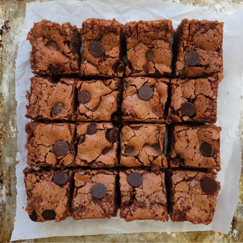 chocolate fudge banana brownies with dark chocolate chips. top down view of brownies cut into 16 squares on a baking tray. 