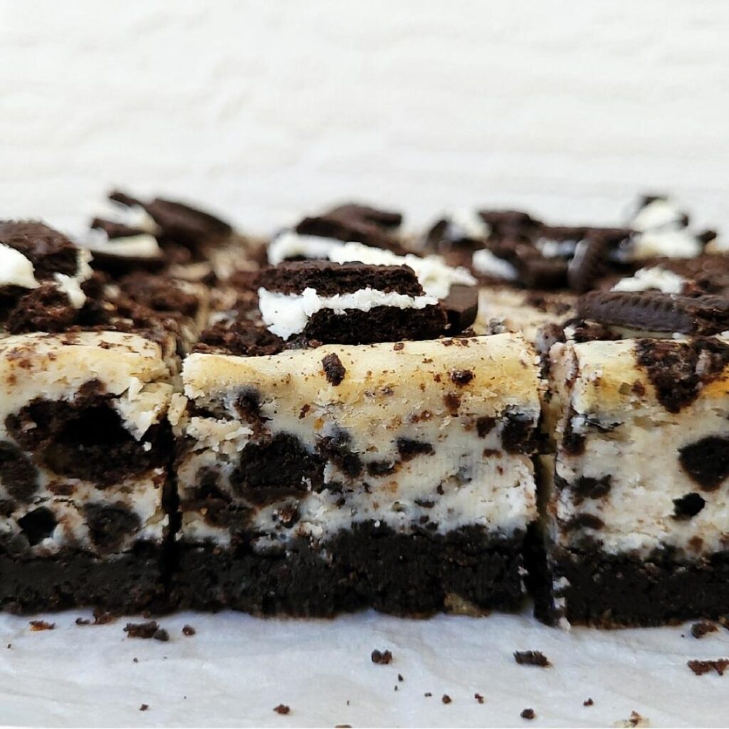 side view of oreo cheesecake bars cut into squares and topped with broken Oreo cookies. 