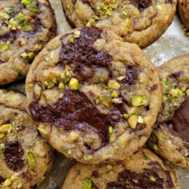 pistachio cookies. top down close up view of cookies topped with chopped pistachios and melted puddles of dark chocolate.