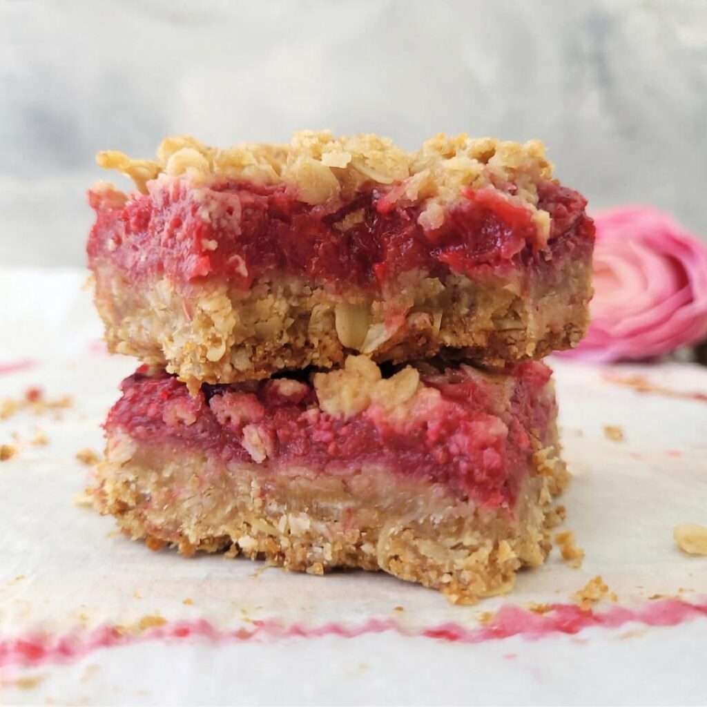 raspberry streusel bars with oat topping. two slices stacked on top of each other with a pink rose in the background. 