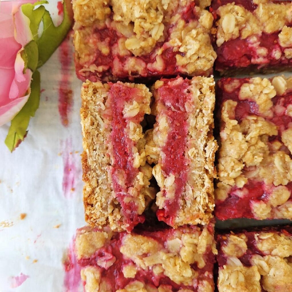 raspberry streusel bars. top down view of oat bars with one slice cut in half and standing on its side so you can see the layers of oats and raspberry jam
