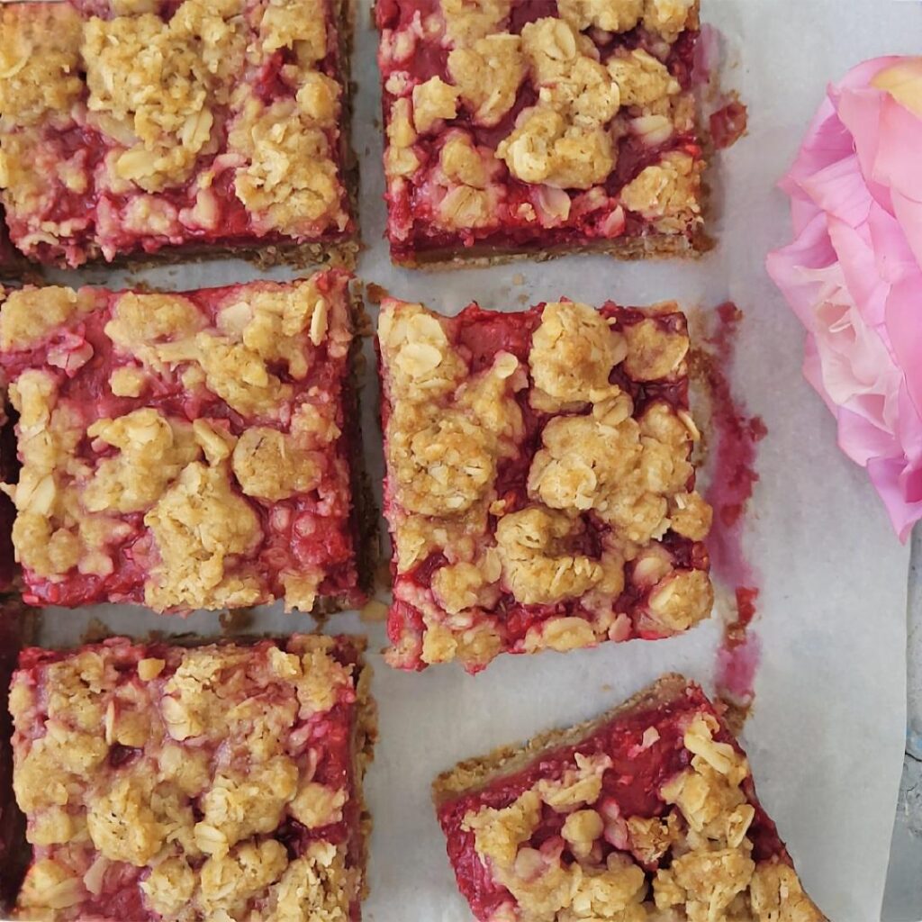 top down view of 6 cut squares of raspberry streusel bars so you can see the buttery oat topping and raspberry jam filling. 